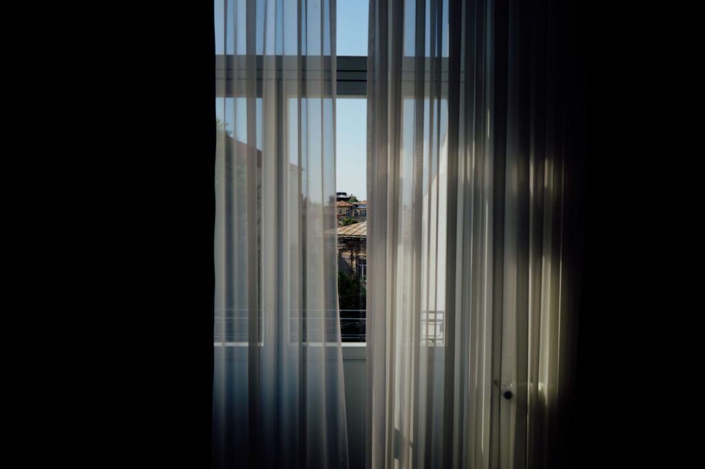 View of the outside through sheer curtains framing a sunny urban landscape.