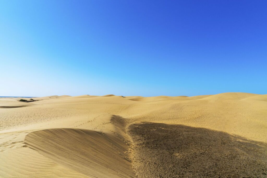 Explore the tranquility of expansive desert sand dunes under a clear blue sky, an image for Can Existence Come Out Of Nothing