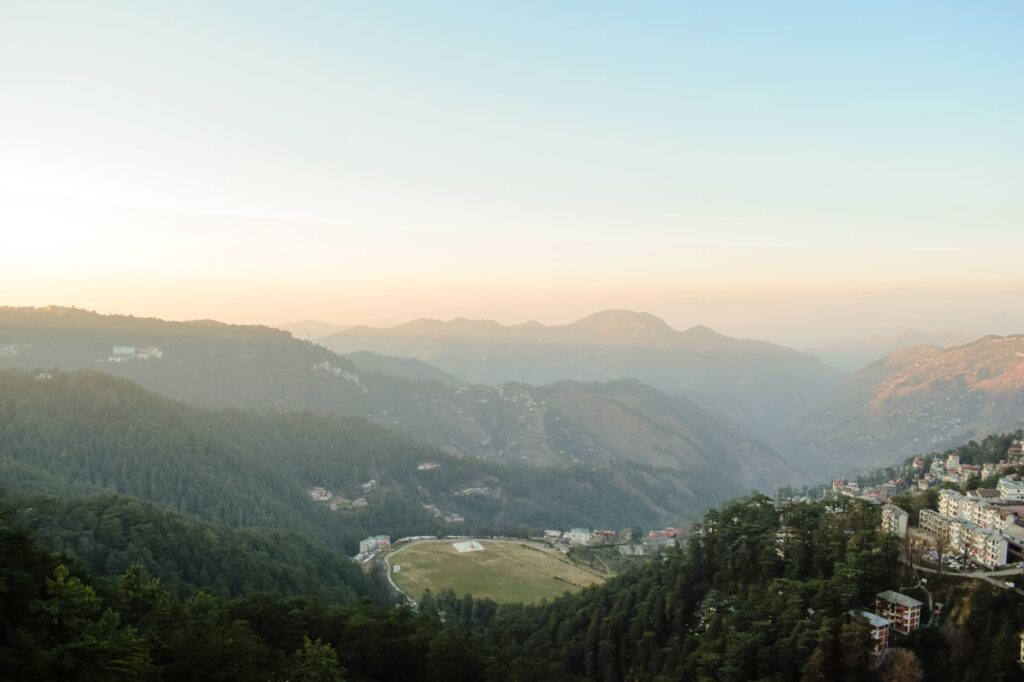 Stunning aerial view of a misty mountain valley at sunrise, capturing the serene landscape with trees and distant cityscape.