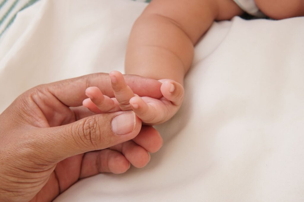 Close-up of a parent's hand gently holding a baby's hand, symbolizing love and care, an image for Create Knowing Suffering Would Follow? Why God Made Humanity