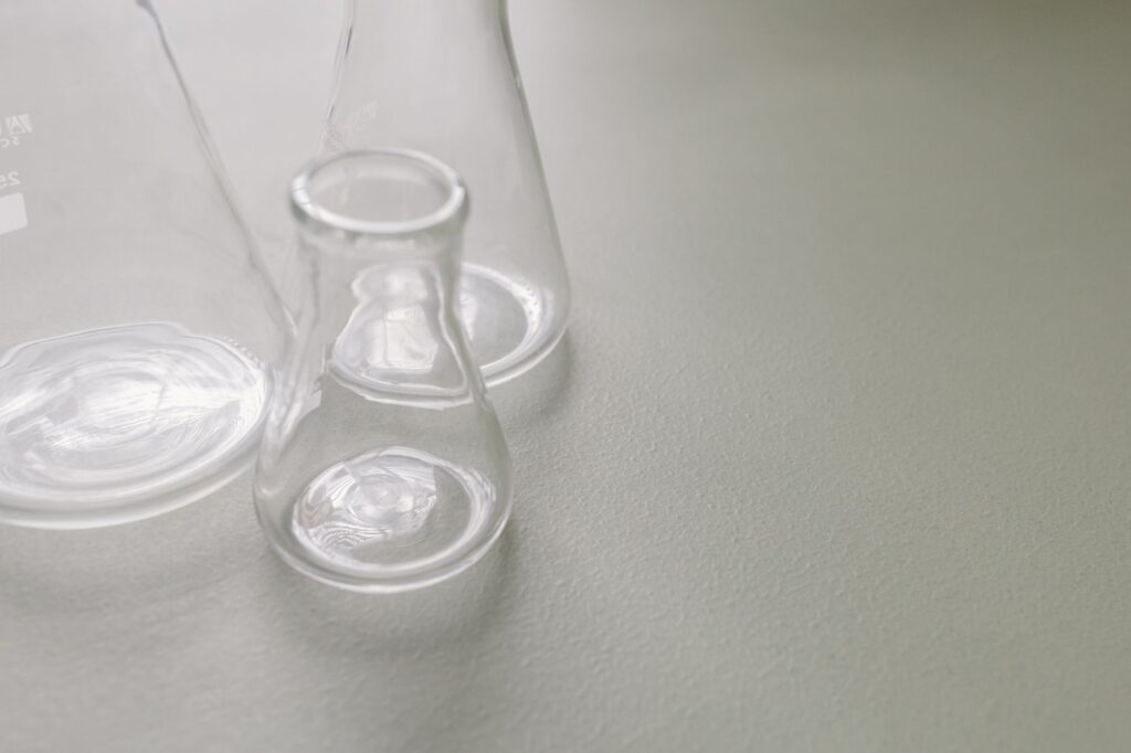 Close-up of clear Erlenmeyer flasks on a light-colored surface, ideal for scientific concepts.