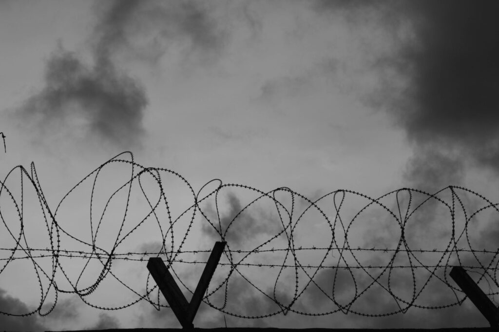 A dramatic black-and-white image showing barbed wire silhouetted against a cloudy sky.