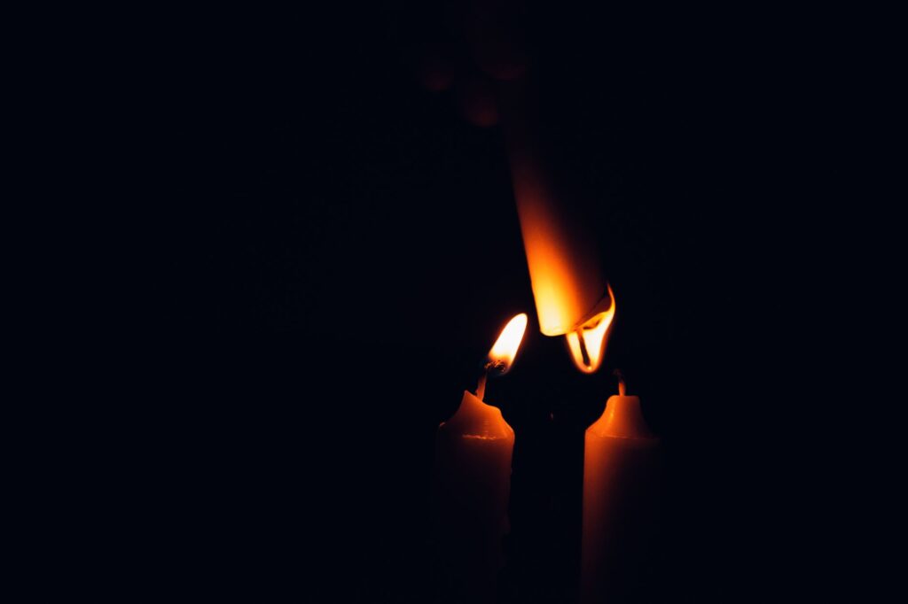 Close-up of candle flames against a dark background, offering warm illumination, an image for When the Presence Fades