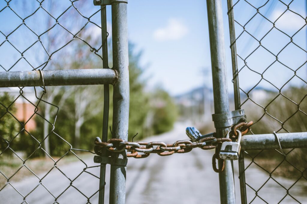 Close-up of a locked chain link fence with rusty chains and padlock, outdoors, in bright daylight.
